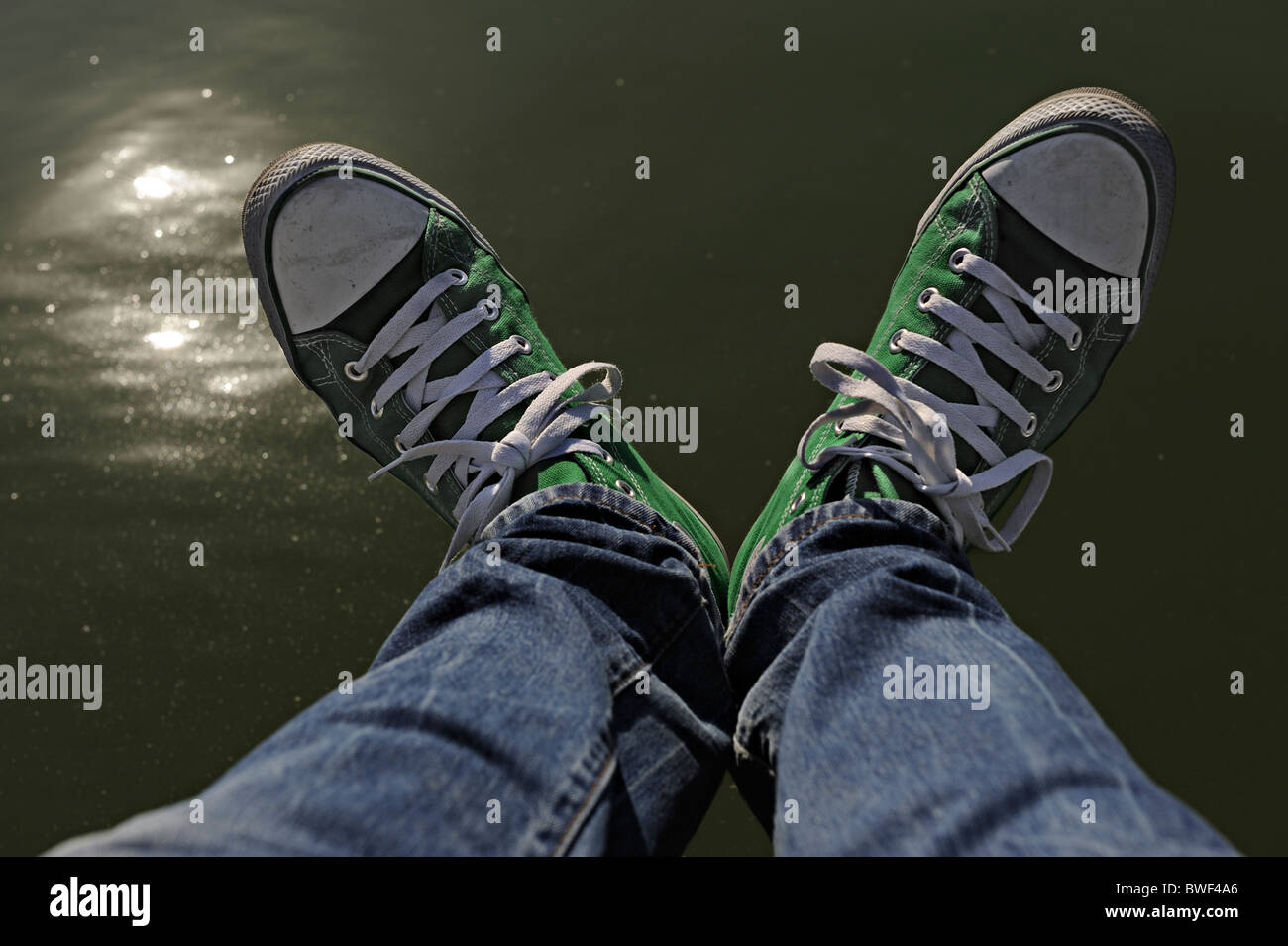 Piernas con blue jeans y zapatillas Converse verdes sentado encima del agua  Fotografía de stock - Alamy