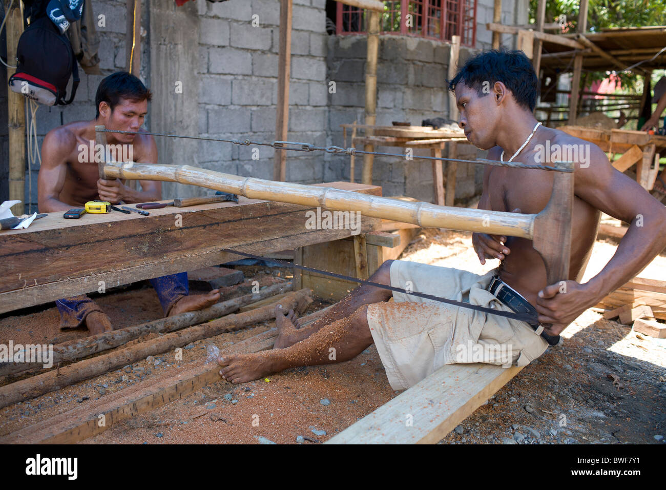 Obreros filipinos equipo vio un grueso trozo de madera narra en tablones en Mansalay, Mindoro Oriental, Filipinas. Foto de stock