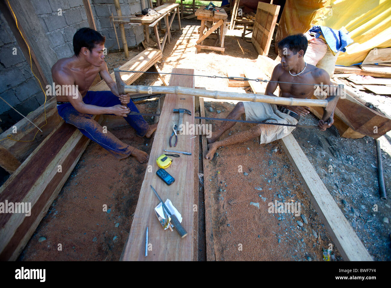 Obreros filipinos equipo vio un grueso trozo de madera narra en tablones en Mansalay, Mindoro Oriental, Filipinas. Foto de stock