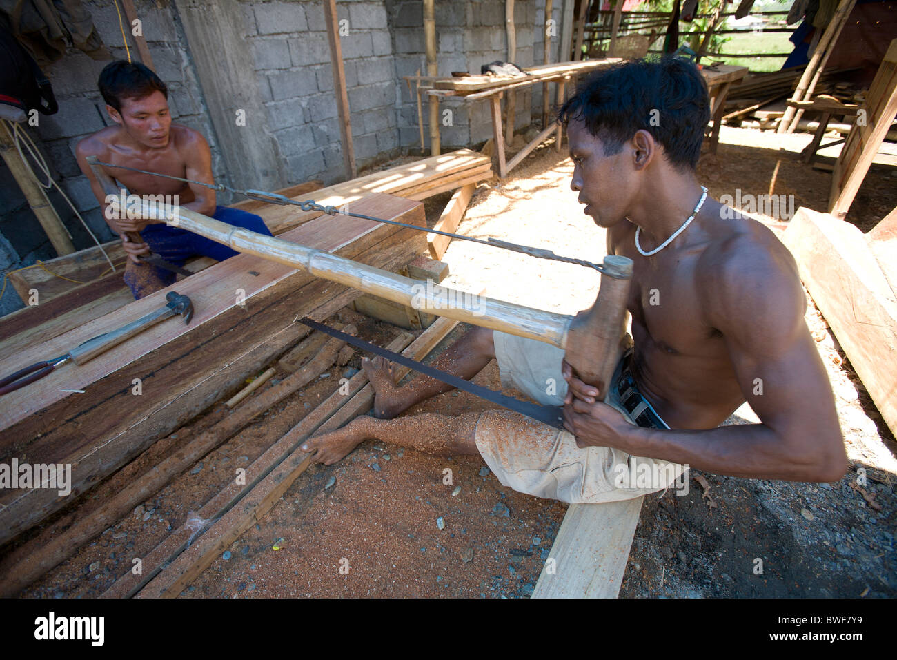 Obreros filipinos equipo vio un grueso trozo de madera narra en tablones en Mansalay, Mindoro Oriental, Filipinas. Foto de stock