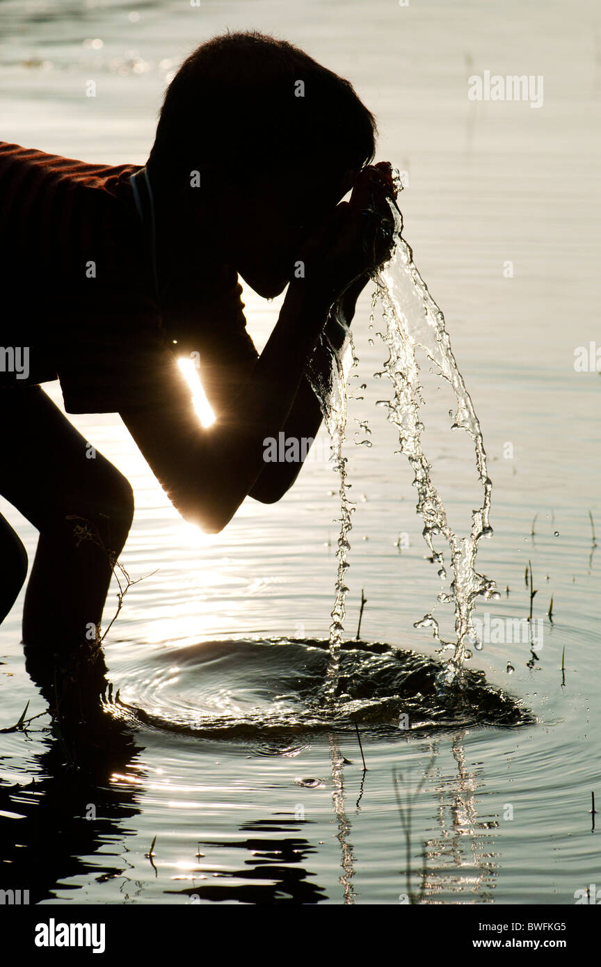 Niño Indio y lavar en agua potable en la India un lago al atardecer. Silueta. En Andhra Pradesh, India Foto de stock