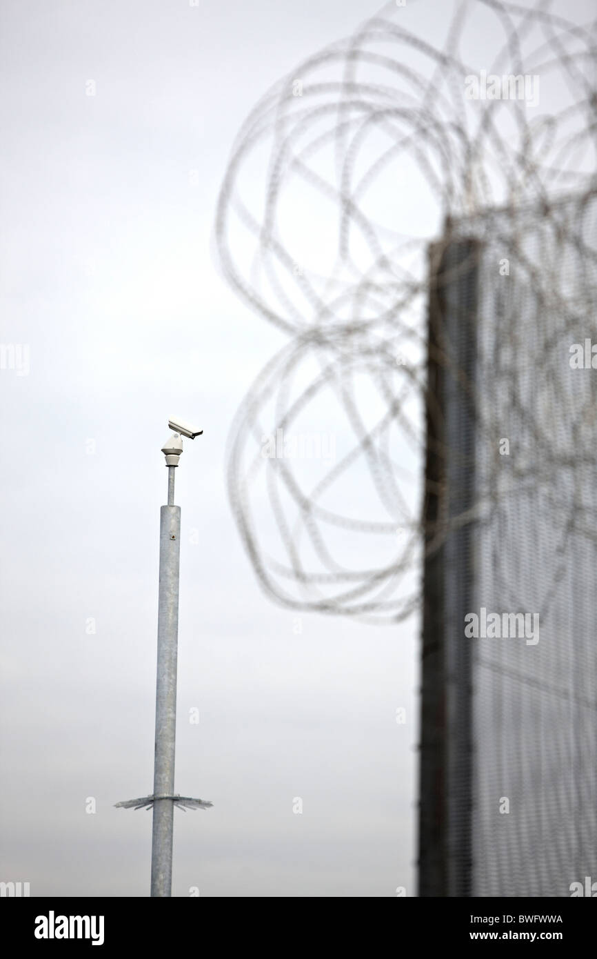 Cámara de seguridad CCTV y una alta alambrada fuera una instalación segura. Foto de stock