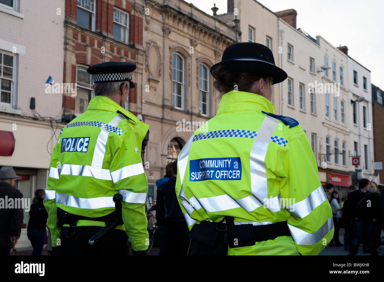 Mujer Policía oficial de apoyo comunitario caminando por el centro de la ciudad de Hereford, Reino Unido. Vista trasera de la hembra con PEP colega masculino. Foto de stock