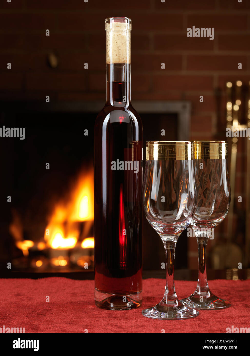 Botella de vino seco de color rojo y dos copas de vino en una tabla con una chimenea en el fondo Foto de stock