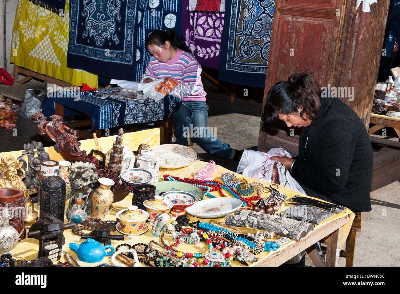 Las mujeres bordar junto a puesto en el mercado, Baisha Village, cerca de Lijiang, provincia de Yunnan, China Foto de stock