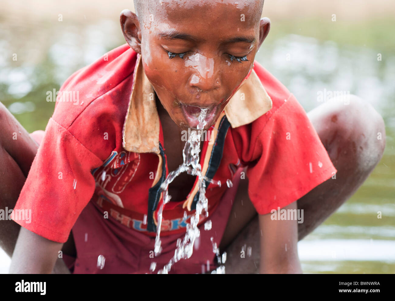 Niño de la calle indio lavarse a sí mismo y a beber agua en un río en la India rural. En Andhra Pradesh, India Foto de stock