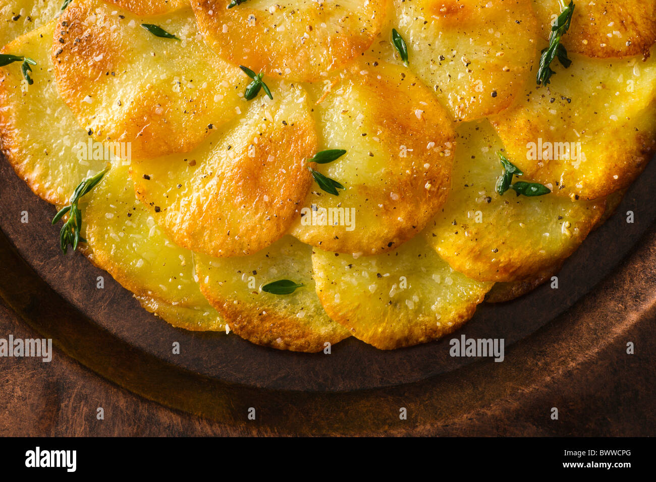 Tortas de patata o Anna aderezado con tomillo fresco, sal y pimienta y se sirve en un plato rústico. Foto de stock