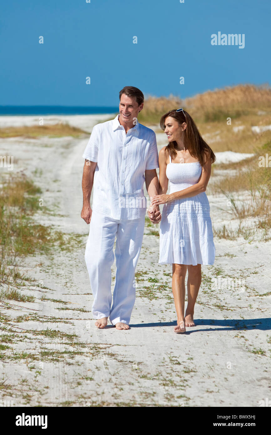 Hombre y mujer pareja romántica ropa blanca tomados de la mano y caminando en una playa desierta con brillante cielo azul claro Fotografía de stock - Alamy
