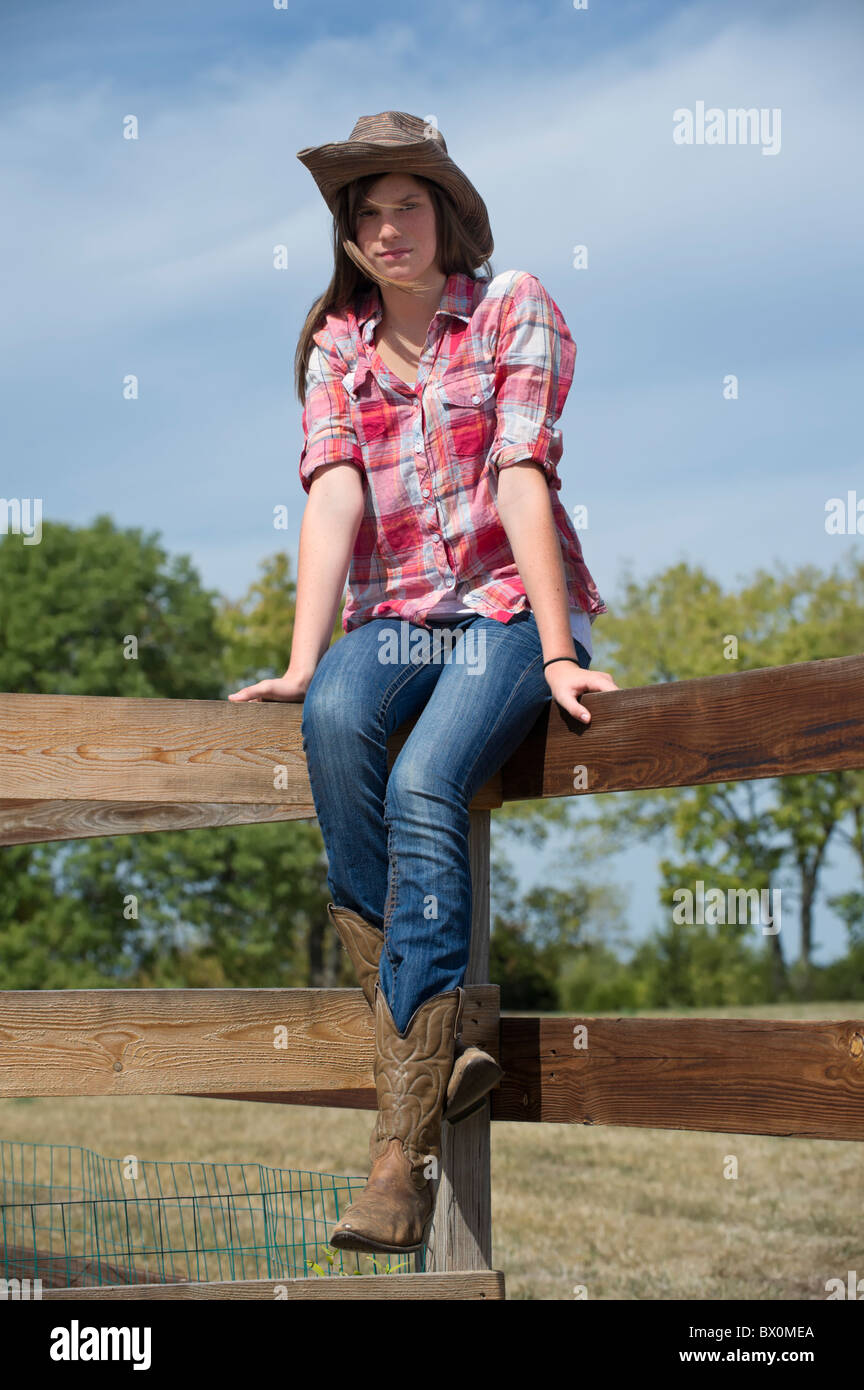 Country Girl adolescente sentado en el raíl valla en vestimenta casual,  sombrero de cowboy y botas, pantalones vaqueros y camisa de cuadros  escoceses Fotografía de stock - Alamy