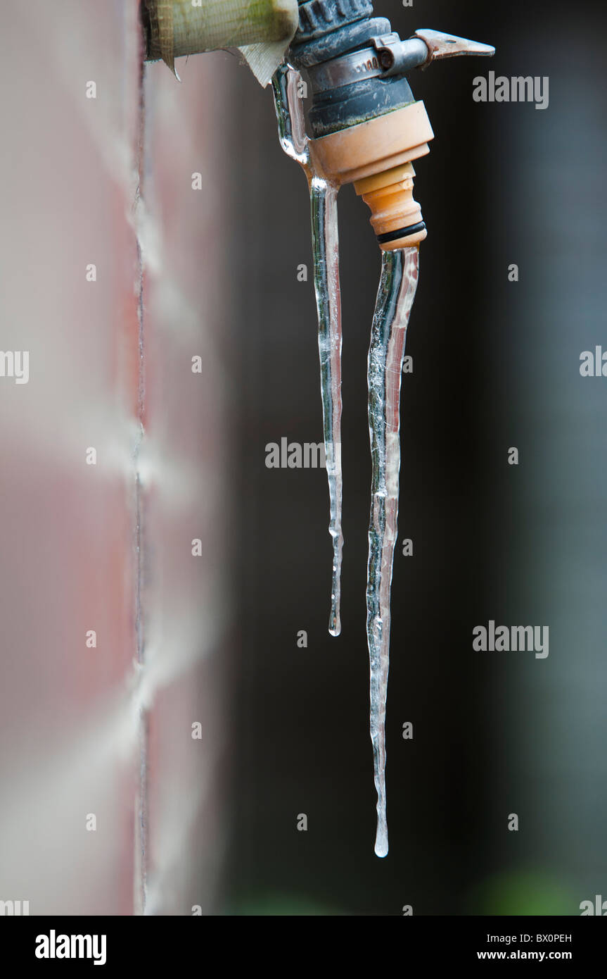 Goteo del grifo con hielo congelado contra la pared de la casa Foto de stock