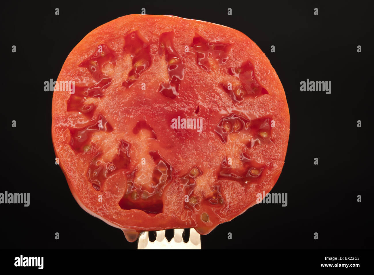 Un corte jugoso tomate, está sentado sobre un fondo negro Foto de stock