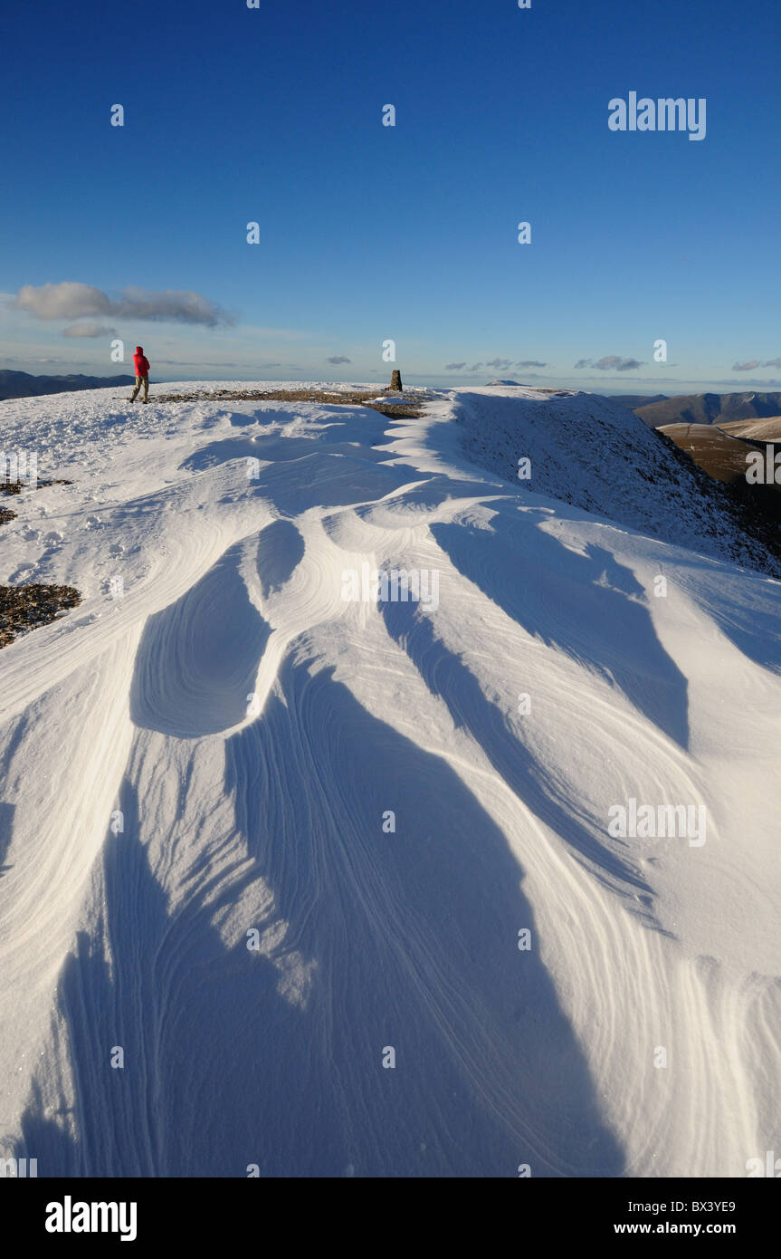 El viento sopla nieve esculpidas patrones y Walker en la cumbre de Helvellyn en el distrito inglés de Lake District. Foto de stock