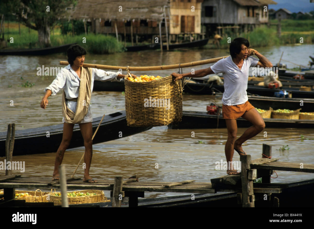 Dos hombres desembarcar desde un barco con cestas llenas de tomates en el Lago Inle, Nyaung Shwe, Birmania. Foto de stock
