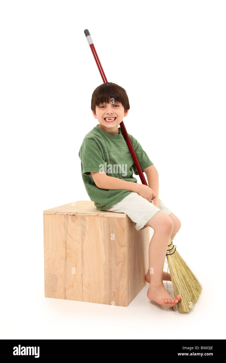Atractivo francés 7 años american muchacho sentado en la caja con su escoba sobre fondo blanco. Foto de stock