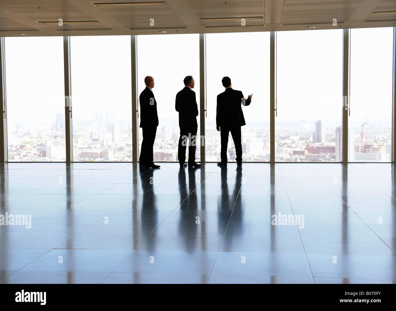 Tres ejecutivos mirando el paisaje de la ciudad en espacio de oficinas vacío Foto de stock