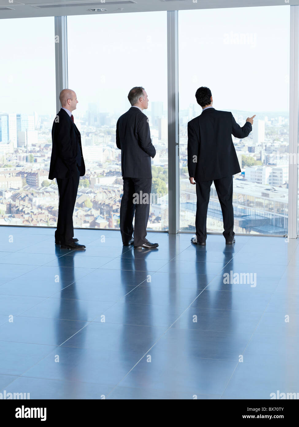Tres ejecutivos mirando el paisaje de la ciudad en espacio de oficinas vacío Foto de stock