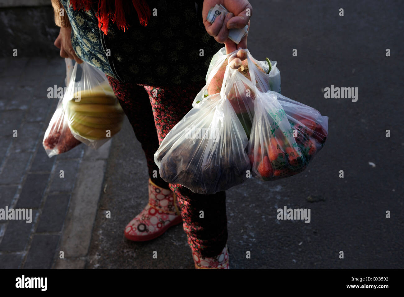 Una mujer lleva las bolsas del supermercado de vuelta a casa después de ir de compras en un mercado de Pekín, China.11-Dec-2010 Foto de stock
