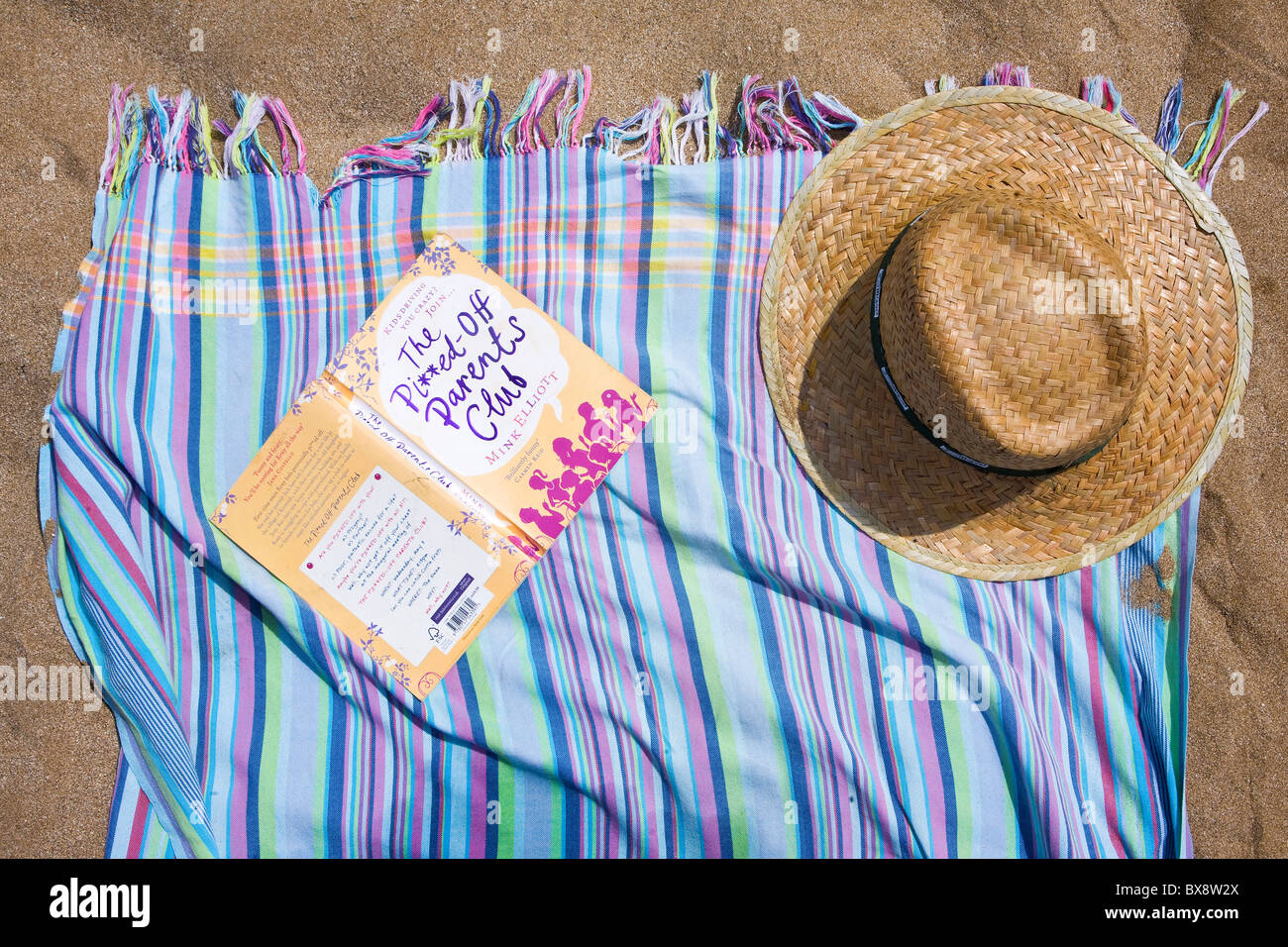 Rayas creemos toalla o sarong con sombrero de paja y la novela de verano Foto de stock