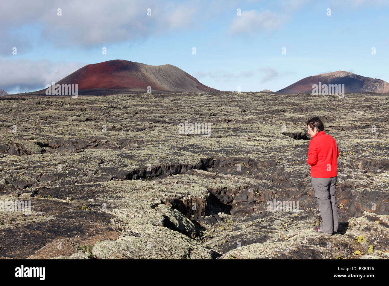 Caldera Colorada y Montaña Ortiz volcanes, mujer de pie en un campo de lava con líquenes, Lanzarote, España, Europa Foto de stock