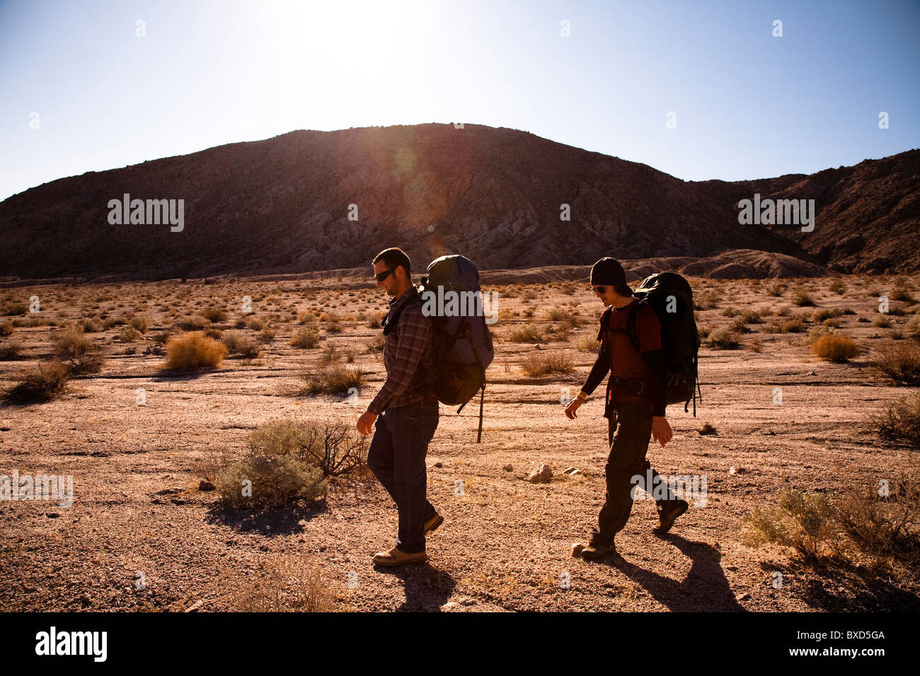 Durante el calor del sol de mediodía, dos varones de excursionistas mochila a través del Valle de la muerte la confianza Hills, California. Foto de stock