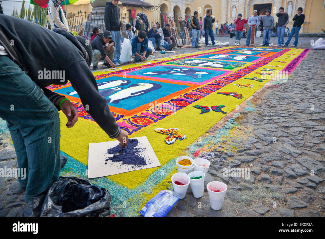 Antigua, Guatemala. Finalizando un borde de mariposas sobre una alfombra de aserrín de colores que representan los temas ambientales. Foto de stock