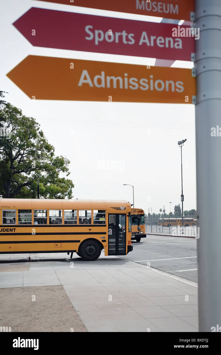 Un autobús escolar amarillo en una intersección con signos que apuntan a la sports arena y admisiones. Foto de stock