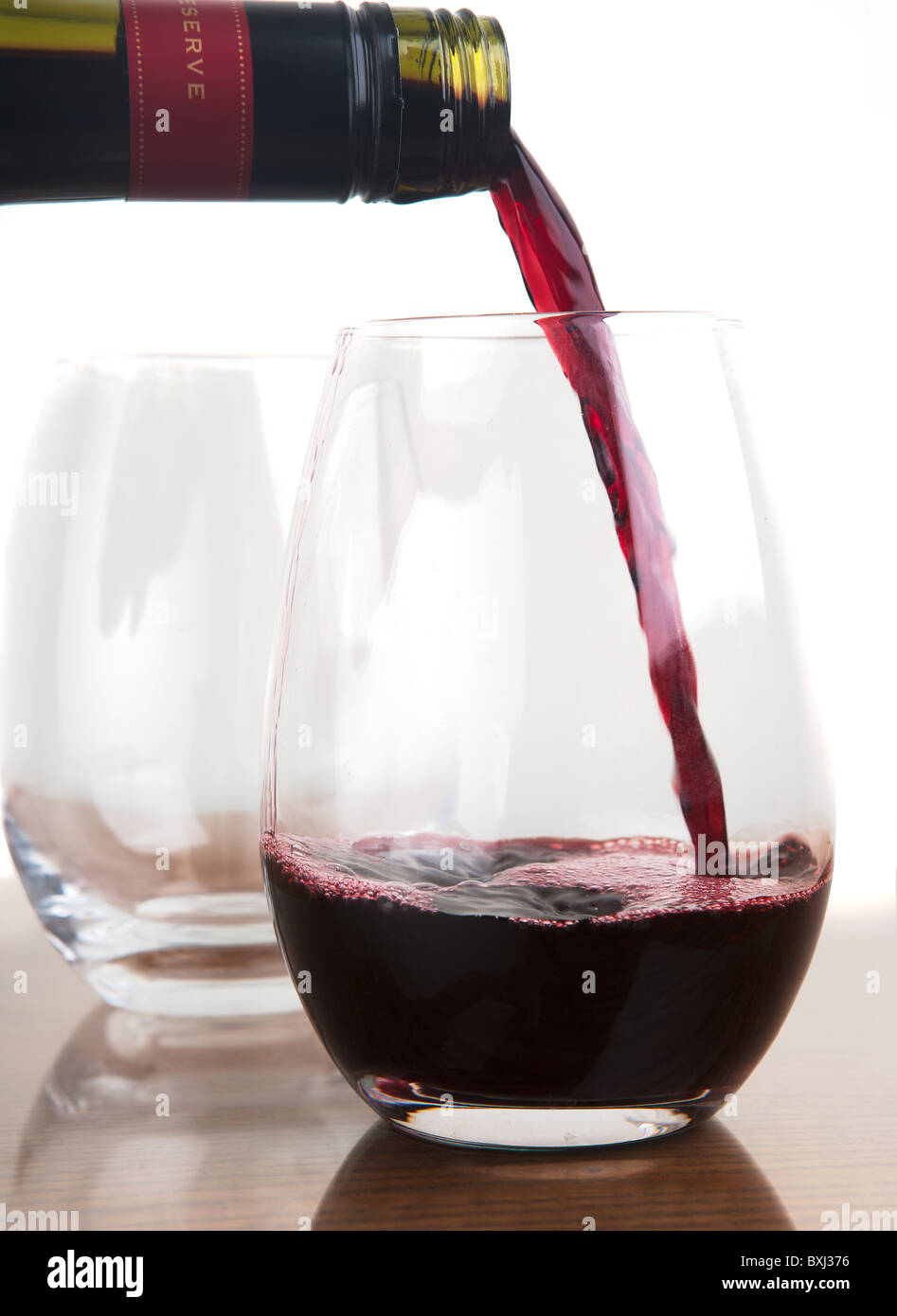 El vino tinto se vuelcan hacia stemless vaso de vino con una segunda copa de vino blanco en el fondo. Foto de stock