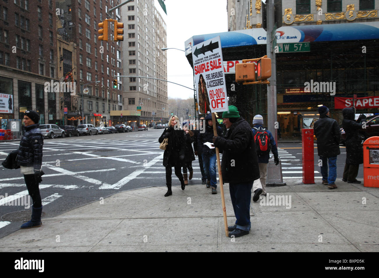 Un viejo hombre sujetando una cartelera de abrigos y chaquetas Shearling venta en la esquina de la Sexta Avenida y 57th st en Blizzard en Manhattan, Nueva York Foto de stock