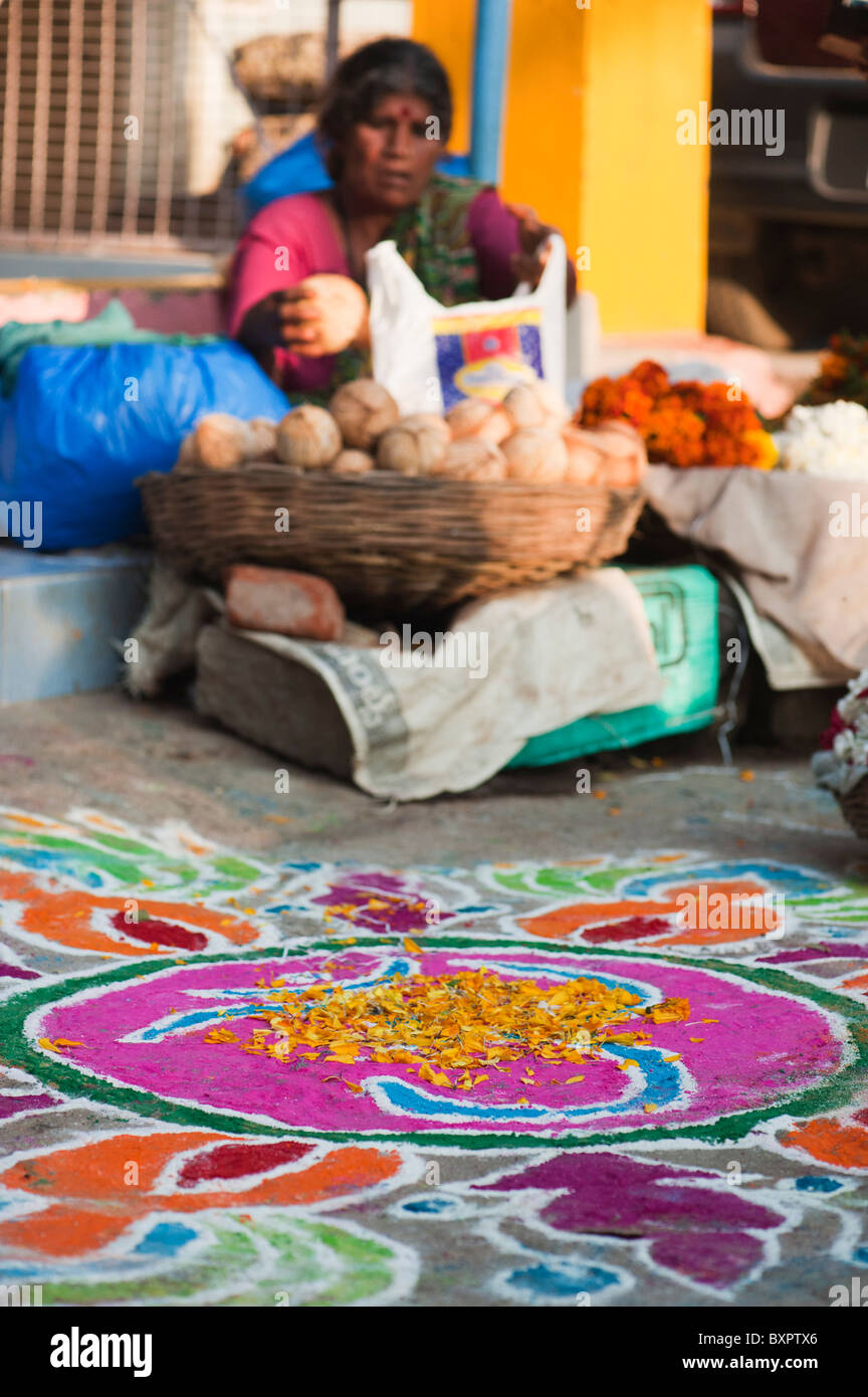 Rangoli sankranti festival coloured powder diseño en una India Street en frente de una mujer vendiendo cocos. En Andhra Pradesh, India Foto de stock