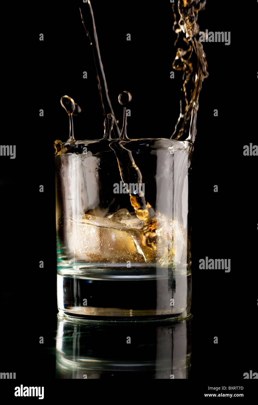 Vaso de Whiskey sobre un fondo negro. Splash Whiskey en un vaso. Whisky con hielo. Foto de stock