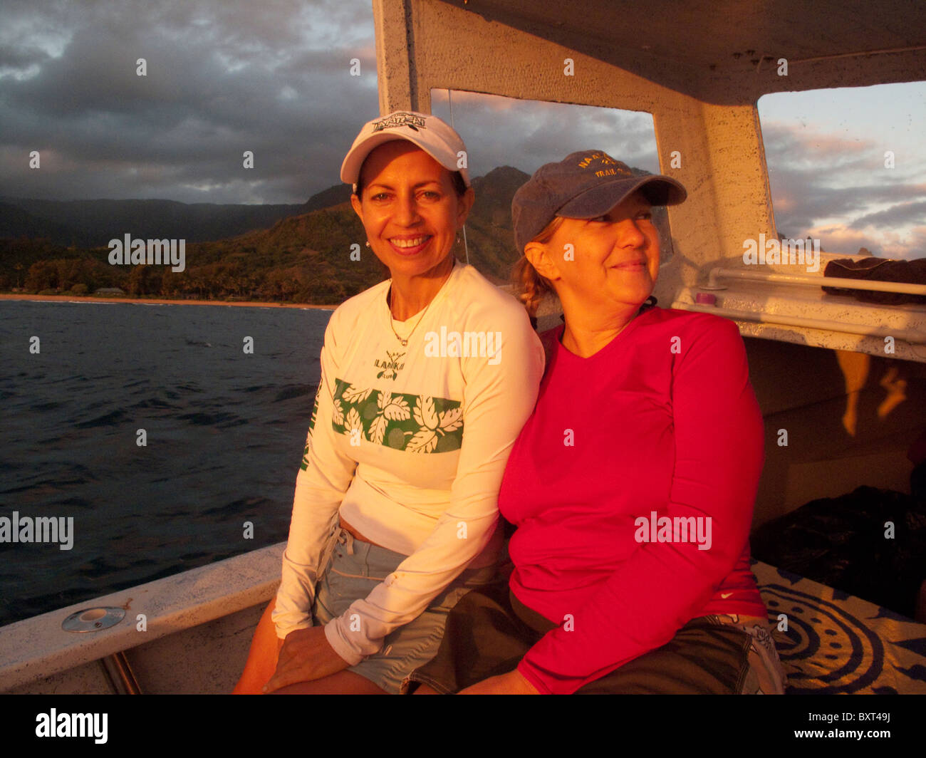 Dos mujeres (edad 50) en bote a lo largo de la costa de Na Pali de Kauai, temprano en la mañana la luz Foto de stock