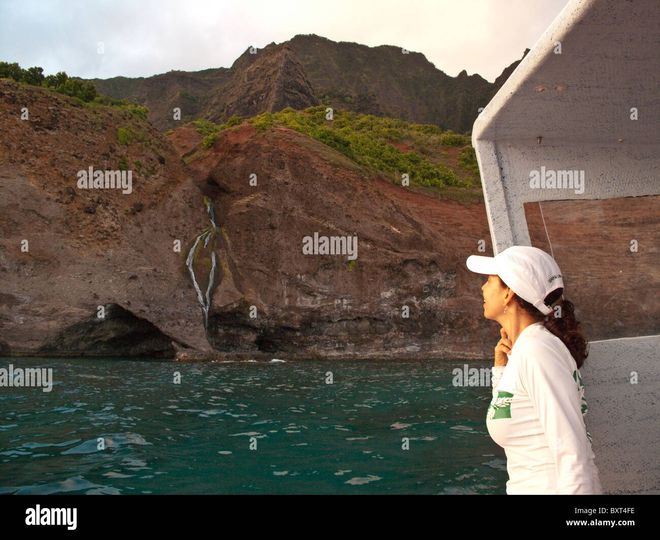 Foto de mujer madura buscando en cascada en la costa Na Pali de Kauai, tomada desde el agua en las primeras horas de la mañana la luz Foto de stock