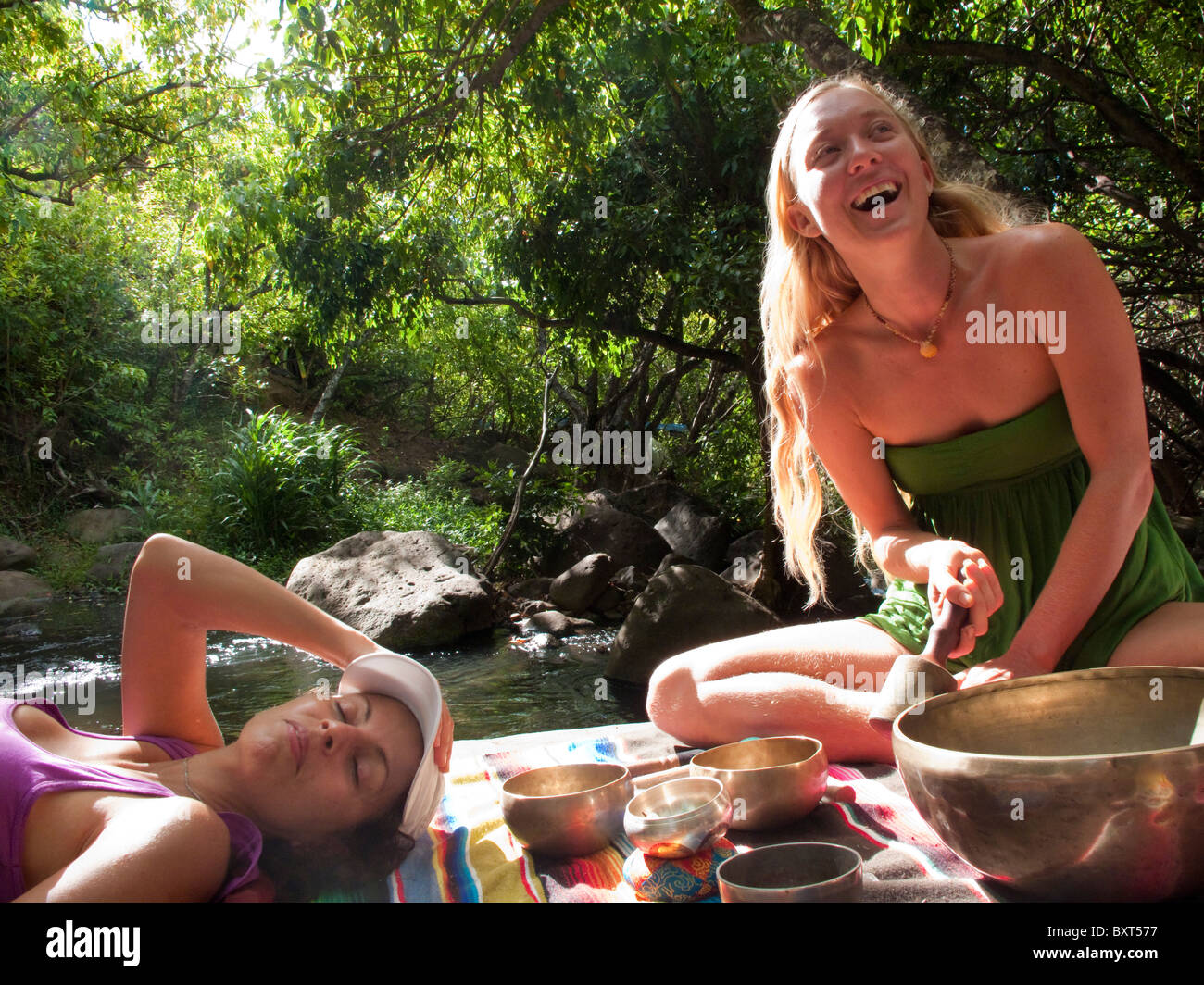 Dos mujeres descansando sobre una gran roca en el Valle Kalalau, mientras escucha el canto cuencos tibetanos para la curación, la costa de Na Pali, Kauai Foto de stock