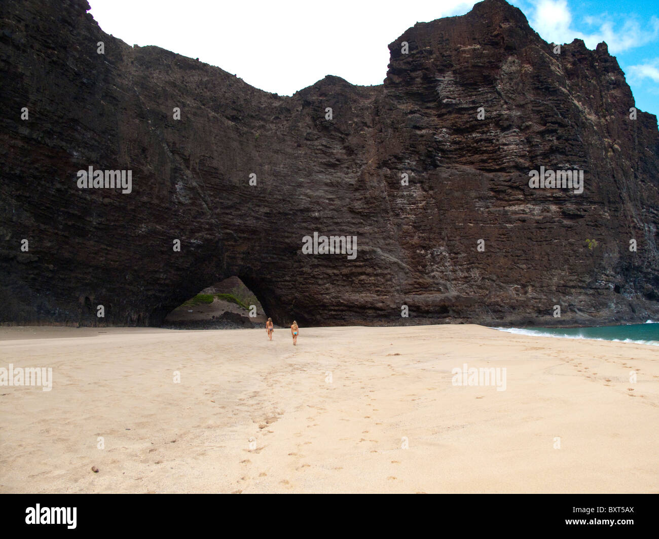Dos mujeres jóvenes caminando hacia el arco, Honopu beach, Costa Na Pali, Kauai Foto de stock