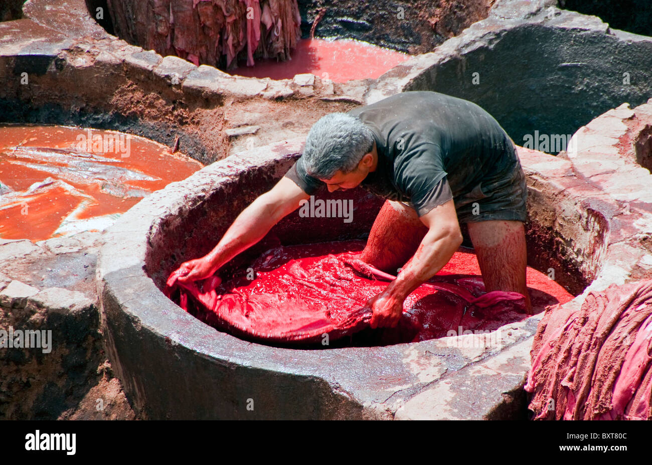 Trabajador de colorante rojo teñido de iva piel animal a ser hecha en zapatillas (babouche) al famoso curtiembres de Fes, Marruecos Foto de stock