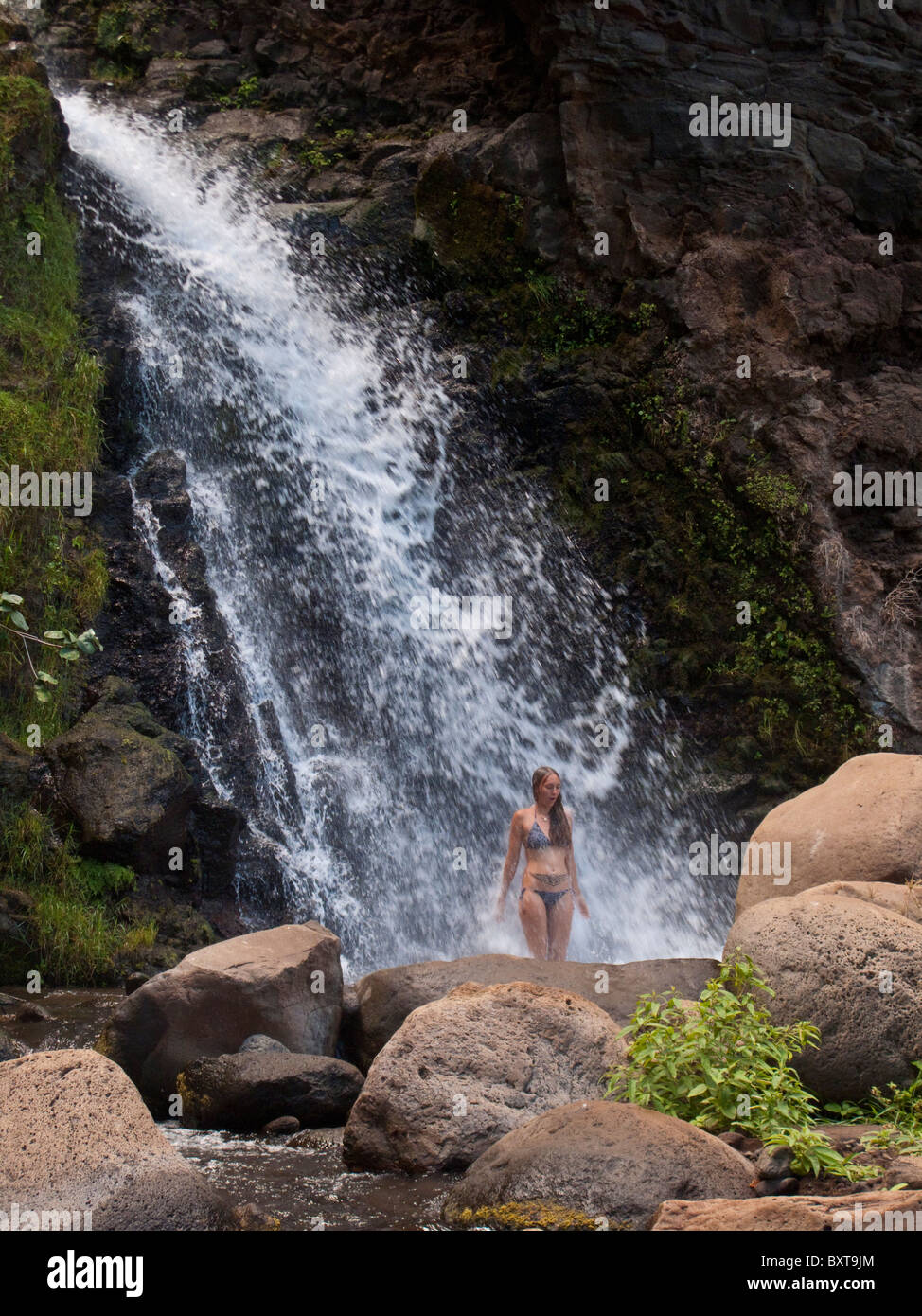 Mujer de pie bajo una gran cascada en Honopu valle cerca de la costa Napali, Kauai Foto de stock