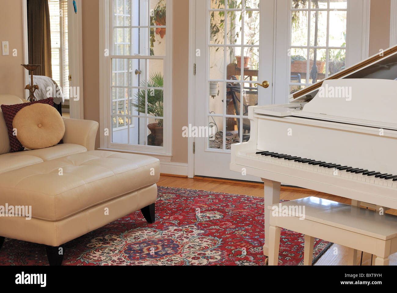 Salón interior contemporáneo con sofá, sillón, piano, y la vista de la ventana del patio. Foto de stock