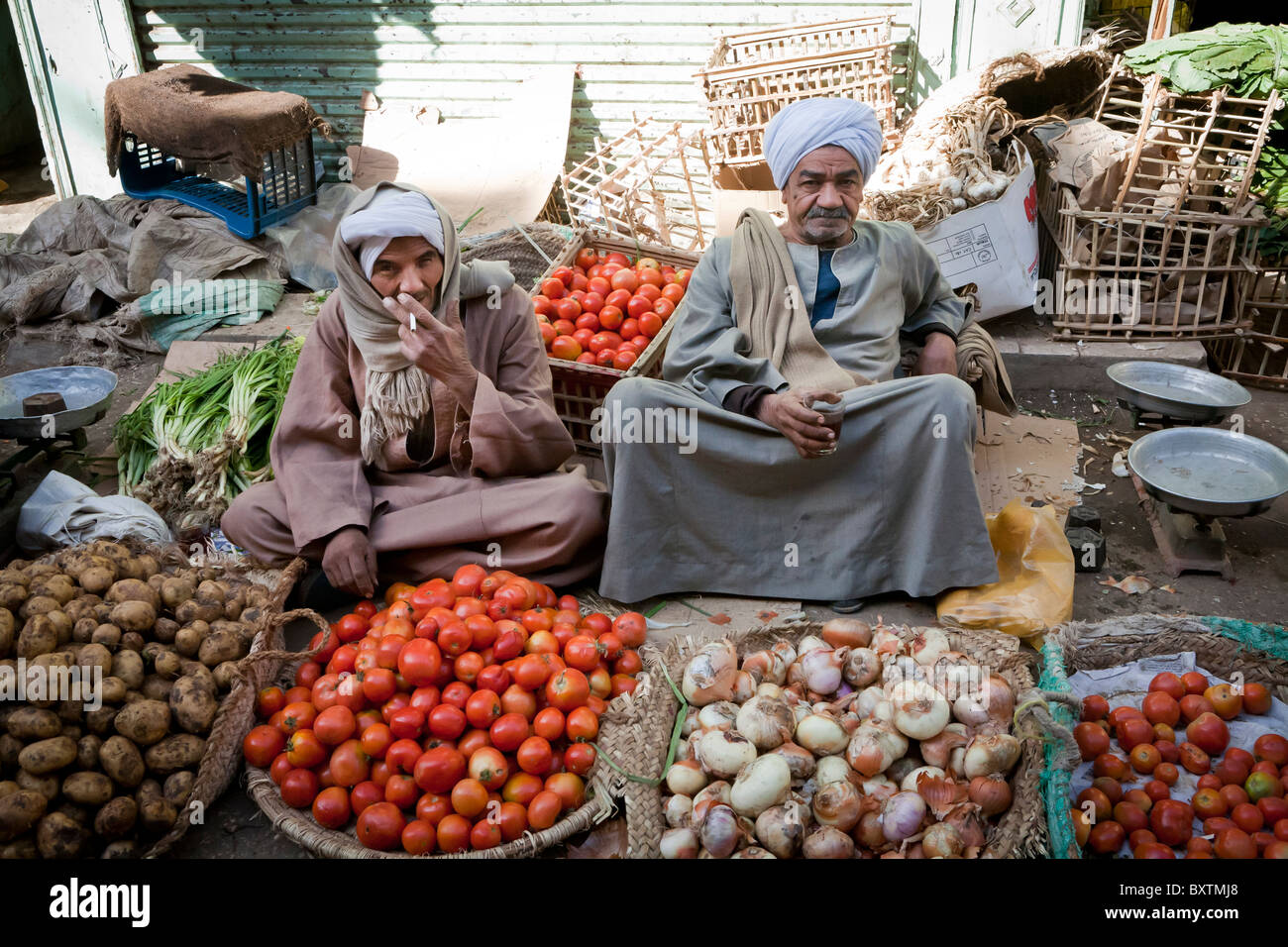 Dos hombres, uno fumar un cigarrillo, sentado en medio de sus verduras en un mercadillo local, Luxor, Egipto, África Foto de stock