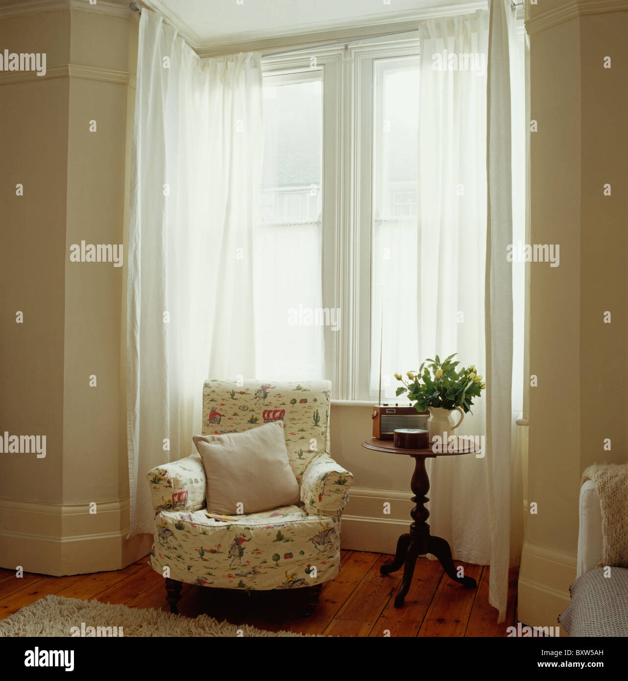 Telas sueltas de cubierta en un sillón junto a la pequeña mesa antigua  delante de ventanas con cortinas de velo blanco Fotografía de stock - Alamy