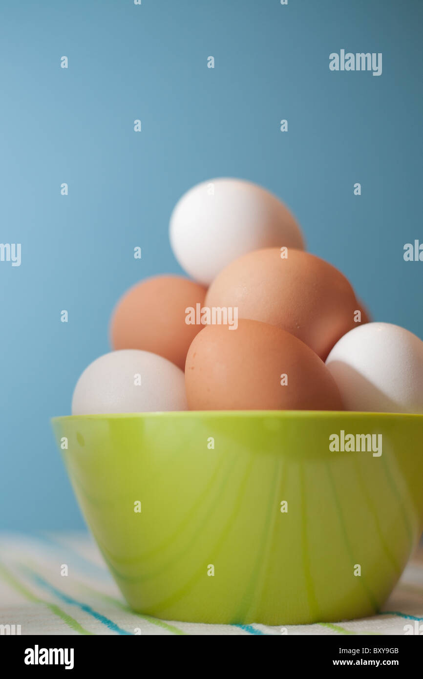 Marrón y blanco de los huevos de pollo en un tazón de rayas verdes sobre un paño de cocina con un fondo azul. Foto de stock