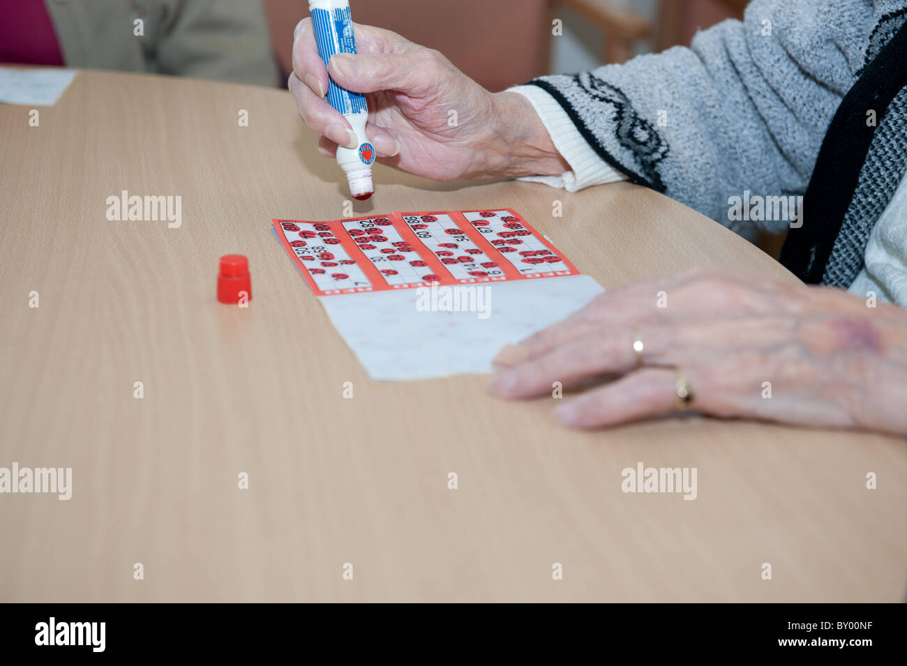 Cerrar la imagen de marca de la mano anciana tarjeta de bingo en la parte superior de la mesa. Foto de stock