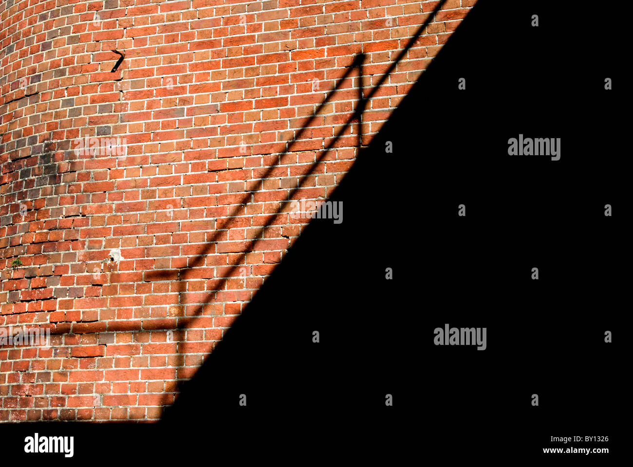 Pasamanos en una empinada escalera exterior lanzando un fuerte sombra a través de una pared de ladrillo Foto de stock