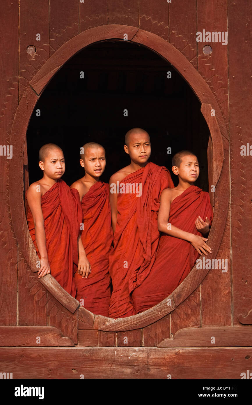 Myanmar, Birmania, Nyaungshwe. Los jóvenes monjes novicios en permanente una ventana oval de madera, Shwe Yaunghwe Kyaung monasterio. Foto de stock