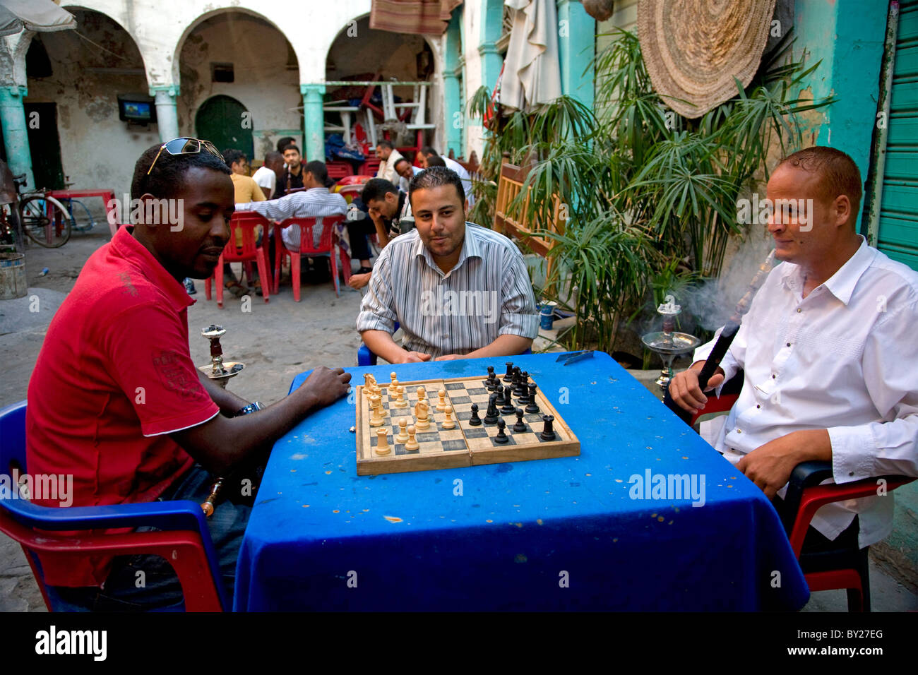Trípoli, Libia; el hombre matar el tiempo jugando cartas, juegos de cartón  y fumar shisha en el patio de un ex "funduq Fotografía de stock - Alamy