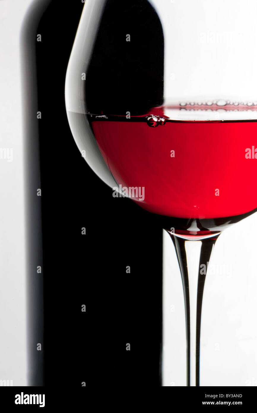 Bodegón con botella y vaso de vino rojo sobre fondo blanco. Foto de stock