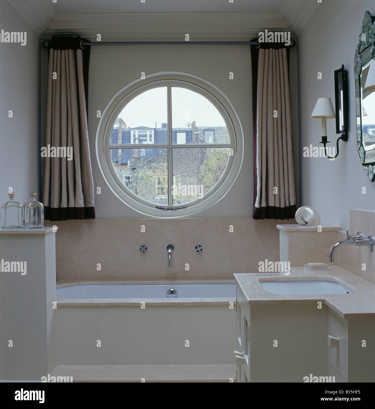 Cortinas de seda beige en cualquier lado de la ventana circular sobre la  bañera en el cuarto de baño pequeño adosado crema Fotografía de stock -  Alamy