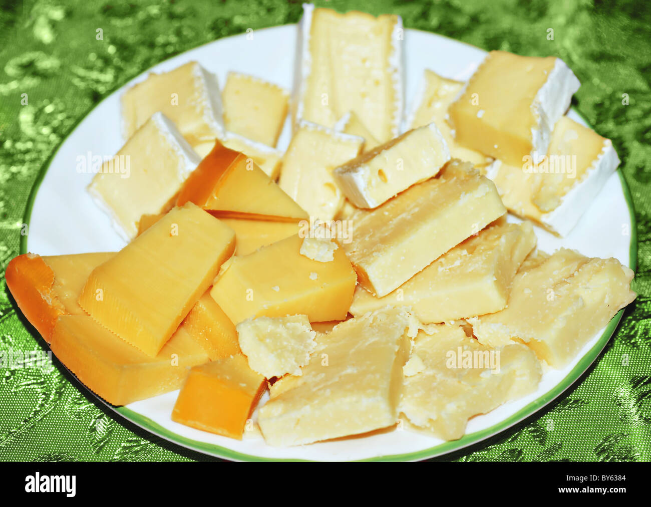 Tabla de quesos, gouda, cheddar viejo y brie sirve sobre una placa blanca sobre el mantel verde. Foto de stock