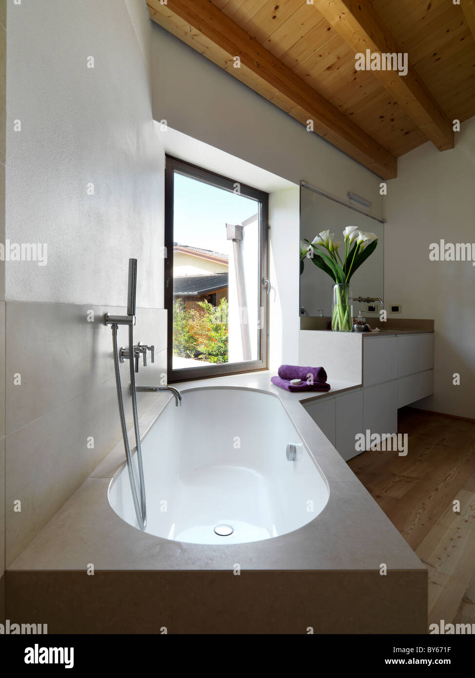 Cuarto de baño moderno con bañera y lavabo en el ático con un techo de vigas de madera Foto de stock