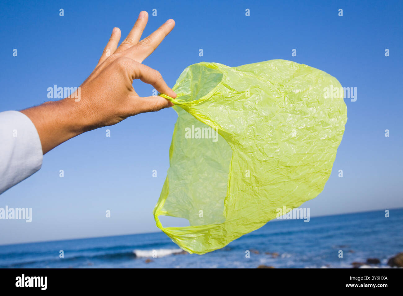 Mano sujetando una espalda verde biodegradable por el mar. Foto de stock