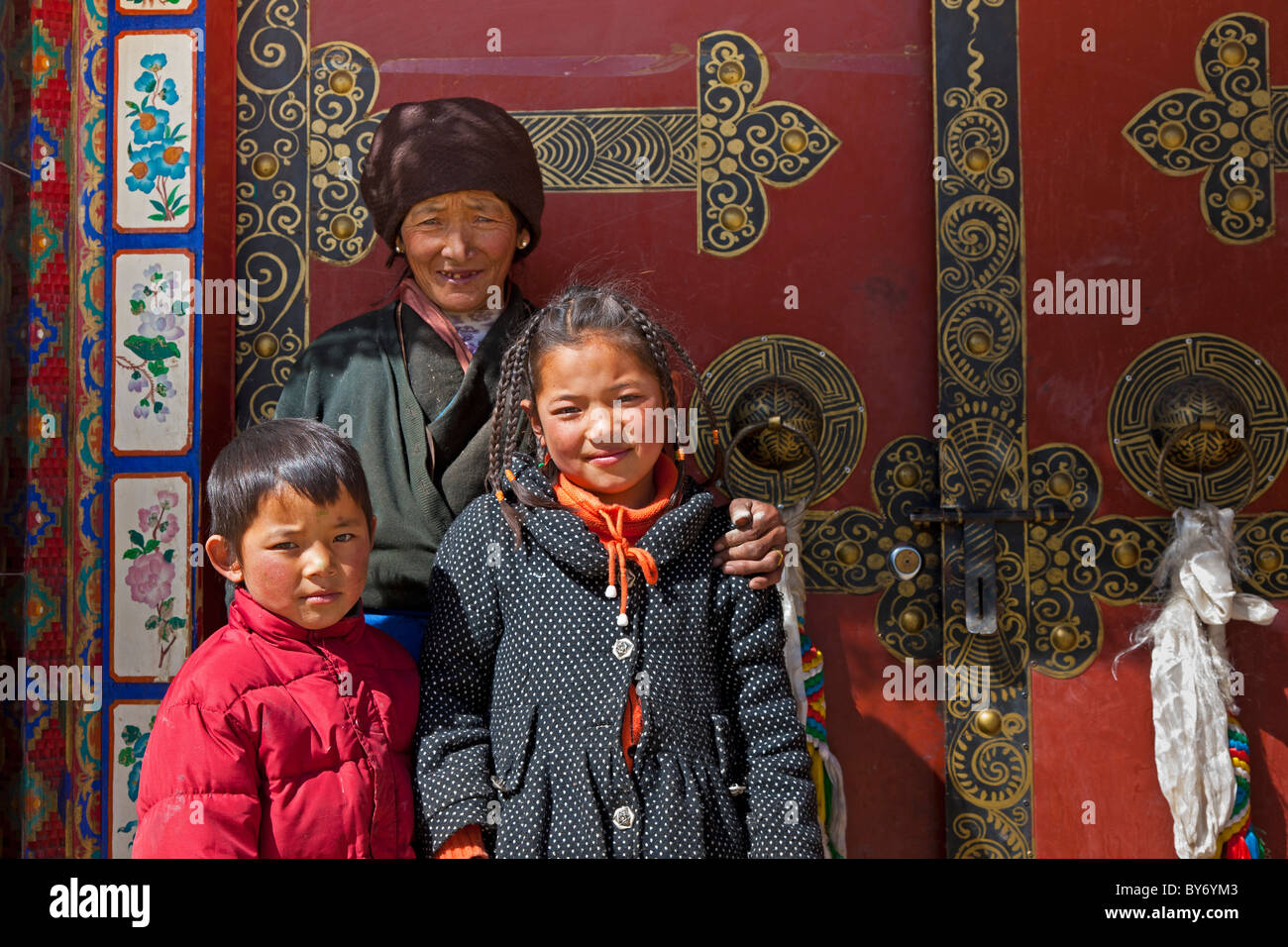 Mujer tibetana chico y chica delante de la entrada a la casa en la aldea tibetana en el camino desde el aeropuerto hasta Lhasa Lhasa (Tíbet). JMH4430 Foto de stock
